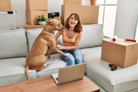 Photo for Young caucasian woman using laptop sitting on sofa with dog at home - Royalty Free Image
