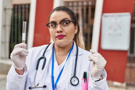 Foto de Young hispanic doctor woman doing coronavirus infection nasal test smiling looking to the side and staring away thinking. - Imagen libre de derechos