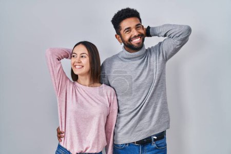 Téléchargez les photos : Young hispanic couple standing together relaxing and stretching, arms and hands behind head and neck smiling happy - en image libre de droit