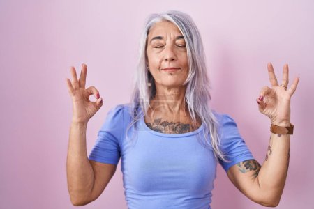 Photo for Middle age woman with tattoos standing over pink background relaxed and smiling with eyes closed doing meditation gesture with fingers. yoga concept. - Royalty Free Image
