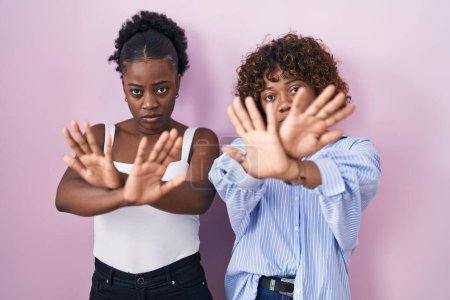 Téléchargez les photos : Deux femmes africaines debout sur fond rose expression de rejet croisant les bras et les paumes faisant signe négatif, visage en colère - en image libre de droit