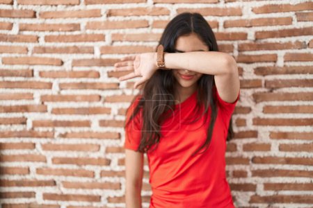 Téléchargez les photos : Young teenager girl standing over bricks wall covering eyes with arm, looking serious and sad. sightless, hiding and rejection concept - en image libre de droit
