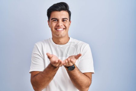 Photo pour Homme hispanique debout sur fond bleu souriant avec les mains paumes ensemble recevant ou donnant geste. maintien et protection - image libre de droit