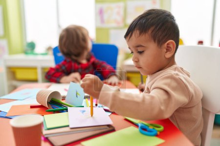 Foto de Dos niños preescolares sentados en la mesa dibujando en papel en el jardín de infantes - Imagen libre de derechos