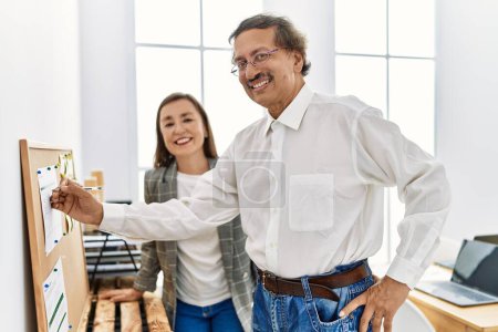 Téléchargez les photos : Homme et femme d'âge moyen travailleurs d'affaires souriant écriture confiante sur le carton-liège au bureau - en image libre de droit