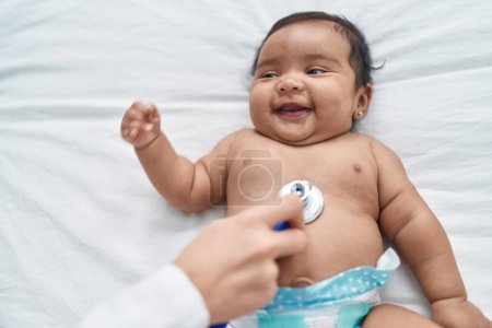 Foto de African american baby smiling confident having medical examination at bedroom - Imagen libre de derechos