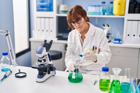 Photo for Middle age woman scientist measuring liquid at laboratory - Royalty Free Image