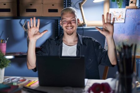 Téléchargez les photos : Young caucasian man using laptop at night at art studio showing and pointing up with fingers number ten while smiling confident and happy. - en image libre de droit