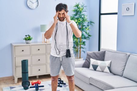 Téléchargez les photos : Handsome latin man wearing sportswear at home with hand on head for pain in head because stress. suffering migraine. - en image libre de droit