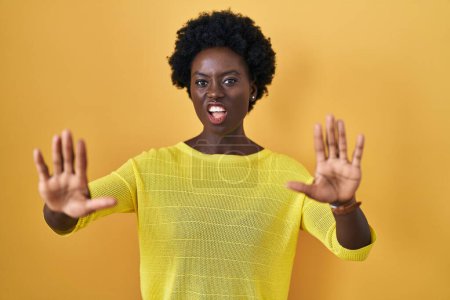 Téléchargez les photos : Jeune femme africaine debout sur le studio jaune faisant geste d'arrêt avec les paumes des mains, expression de colère et de frustration - en image libre de droit
