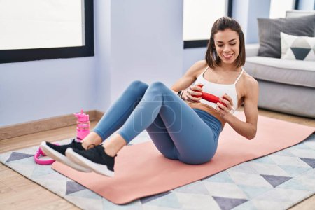 Téléchargez les photos : Young beautiful hispanic woman training abs exercise using dumbbell at home - en image libre de droit