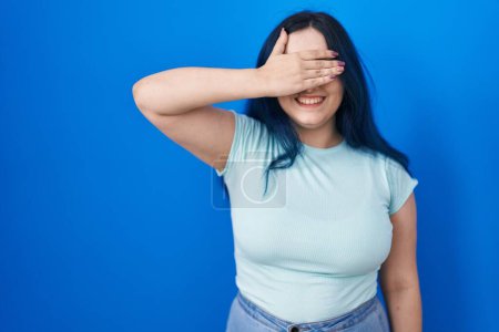Photo for Young modern girl with blue hair standing over blue background smiling and laughing with hand on face covering eyes for surprise. blind concept. - Royalty Free Image