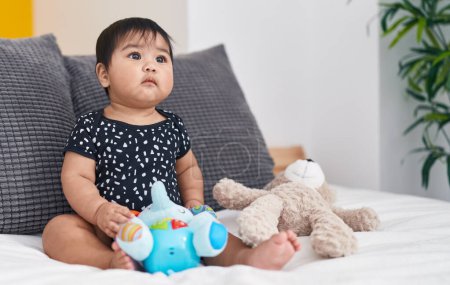 Photo for Adorable hispanic baby playing with dolls sitting on bed at bedroom - Royalty Free Image