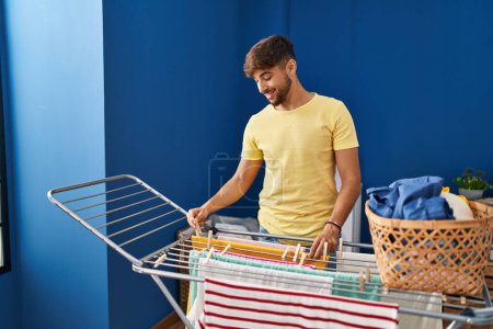 Photo for Young arab man smiling confident hanging clothes on clothesline at laundry room - Royalty Free Image