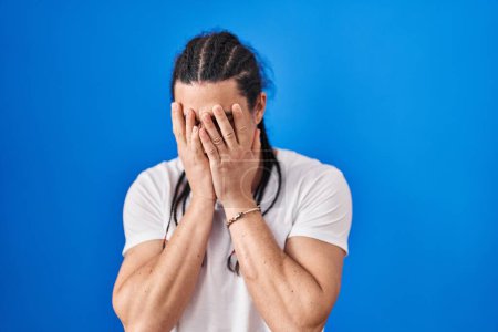 Photo for Hispanic man with long hair standing over blue background with sad expression covering face with hands while crying. depression concept. - Royalty Free Image