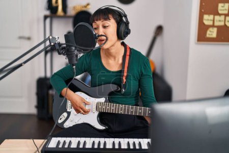 Foto de Young beautiful hispanic woman musician singing song playing electrical guitar at music studio - Imagen libre de derechos