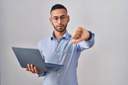 Photo for Young hispanic man working using computer laptop looking unhappy and angry showing rejection and negative with thumbs down gesture. bad expression. - Royalty Free Image