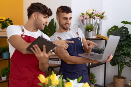 Téléchargez les photos : Two hispanic men florists using laptop and touchpad working at flower shop - en image libre de droit