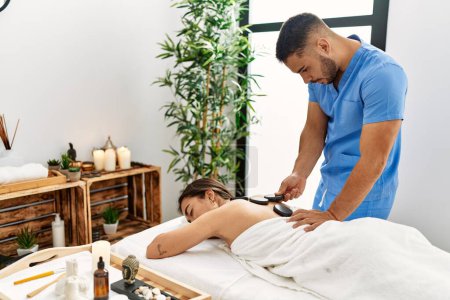Foto de Latino hombre y mujer usando fisioterapia masaje espalda usando piedras calientes en centro de belleza - Imagen libre de derechos