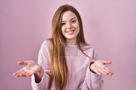 Téléchargez les photos : Jeune femme caucasienne debout sur fond rose souriant joyeuse offrant des mains donnant assistance et acceptation. - en image libre de droit