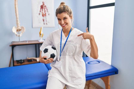 Téléchargez les photos : Jeune femme travaillant à la clinique de thérapie de football pointant du doigt un sourire heureux et fier - en image libre de droit