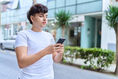 Téléchargez les photos : Homme non binaire utilisant un smartphone avec une expression détendue dans la rue - en image libre de droit