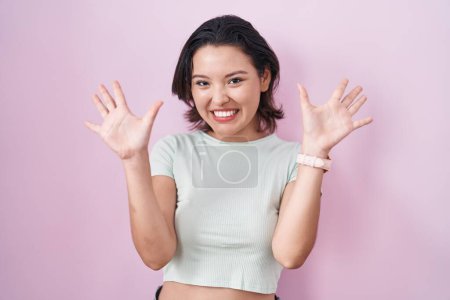 Foto de Hispanic young woman standing over pink background showing and pointing up with fingers number ten while smiling confident and happy. - Imagen libre de derechos