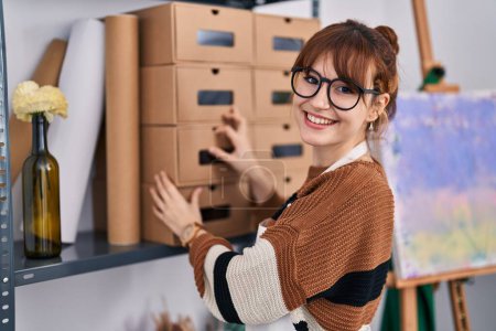 Photo for Young woman artist smiling confident organizing shelving at art studio - Royalty Free Image