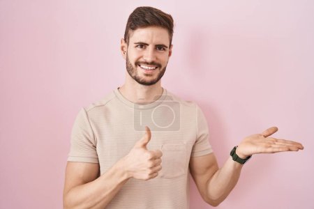 Photo for Hispanic man with beard standing over pink background showing palm hand and doing ok gesture with thumbs up, smiling happy and cheerful - Royalty Free Image