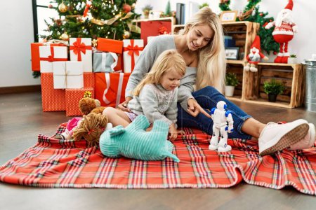 Téléchargez les photos : Mère et fille jouant avec des jouets assis près de l'arbre de Noël à la maison - en image libre de droit