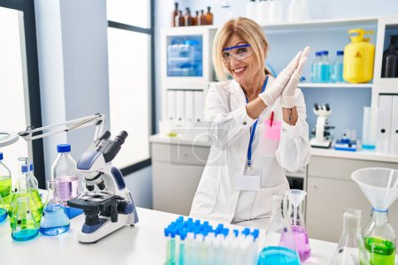 Téléchargez les photos : Femme blonde du moyen âge travaillant au laboratoire scientifique applaudissant et applaudissant heureux et joyeux, souriant mains fières ensemble - en image libre de droit