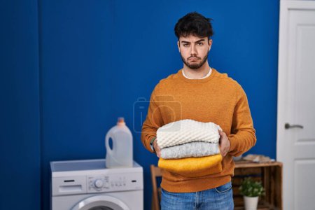 Photo for Hispanic man with beard holding clean folded laundry depressed and worry for distress, crying angry and afraid. sad expression. - Royalty Free Image