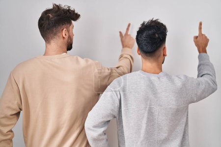 Téléchargez les photos : Jeune couple homosexuel debout sur fond blanc posant vers l'arrière pointant vers l'avant avec la main du doigt - en image libre de droit