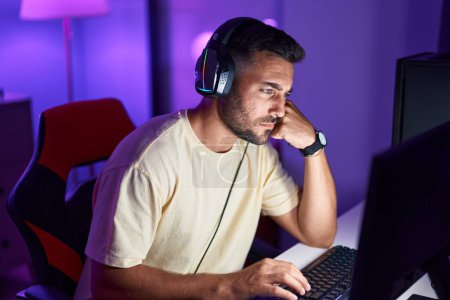 Photo for Young hispanic man streamer sitting on table with serious expression at gaming room - Royalty Free Image