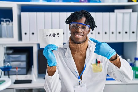 Foto de Joven africano con rastas trabajando en laboratorio científico sonriendo feliz señalando con la mano y el dedo - Imagen libre de derechos