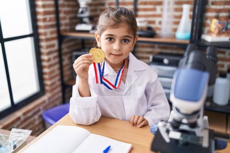 Photo for Adorable hispanic girl student smiling confident holding medal at laboratory classroom - Royalty Free Image
