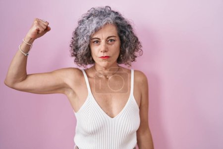 Foto de Mujer de mediana edad con el pelo gris de pie sobre el fondo rosa persona fuerte que muestra el músculo del brazo, confiado y orgulloso de poder - Imagen libre de derechos