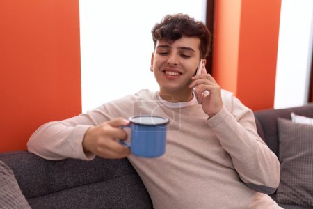 Téléchargez les photos : Non binary man talking on smartphone drinking coffee at home - en image libre de droit
