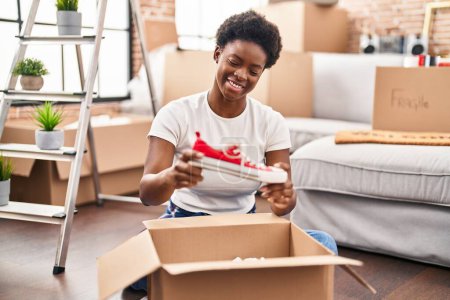 Téléchargez les photos : African american woman unpacking package sitting on floor at new home - en image libre de droit