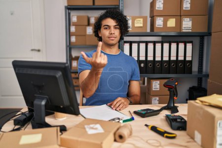 Foto de Hispanic man with curly hair working at small business ecommerce showing middle finger, impolite and rude fuck off expression - Imagen libre de derechos