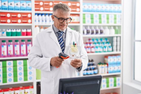 Téléchargez les photos : Middle age grey-haired man pharmacist scanning pills bottle at laboratory - en image libre de droit