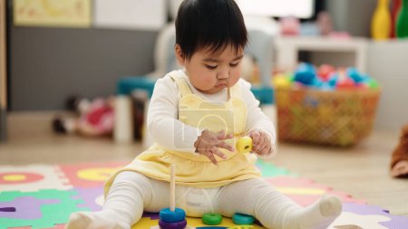 Photo for Adorable hispanic baby playing with hoops sitting on floor at kindergarten - Royalty Free Image