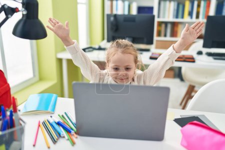 Foto de Adorable estudiante rubia chica usando el ordenador portátil con expresión alegre en el aula - Imagen libre de derechos