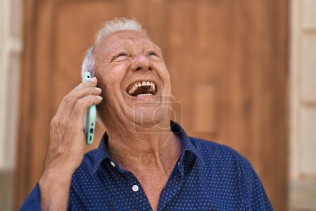 Foto de Senior grey-haired man smiling confident talking on the smartphone at street - Imagen libre de derechos