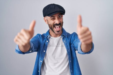 Téléchargez les photos : Homme hispanique avec la barbe debout sur fond isolé approuvant faire un geste positif avec la main, pouces levés souriant et heureux pour le succès. geste gagnant. - en image libre de droit