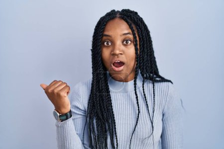 Photo for African american woman standing over blue background surprised pointing with hand finger to the side, open mouth amazed expression. - Royalty Free Image
