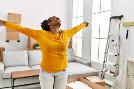 Téléchargez les photos : Femme afro-américaine souriante confiante debout avec les bras ouverts à la nouvelle maison - en image libre de droit