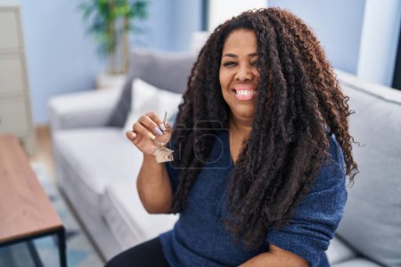 Photo for Plus size hispanic woman holding keys of new home looking positive and happy standing and smiling with a confident smile showing teeth - Royalty Free Image