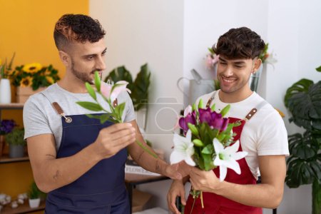 Téléchargez les photos : Two hispanic men florists smiling confident holding bouquet of flowers at flower shop - en image libre de droit