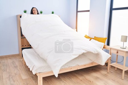 Foto de Joven mujer hispana sonriendo confiada hacer cama en el dormitorio - Imagen libre de derechos